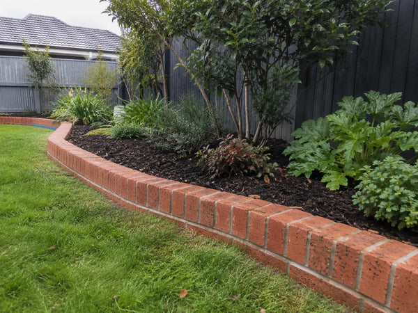 Warm brick garden edging with light-grey mortar around an established garden bed
